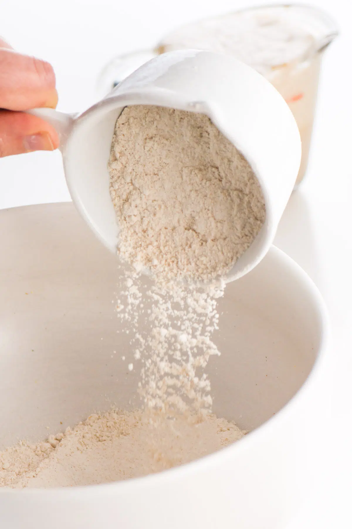 Flour is being poured in a white mixing bowl.
