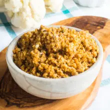 A bowl of Vegan Cauliflower Sausage Crumbles sits on a cutting board in front of raw cauliflower.