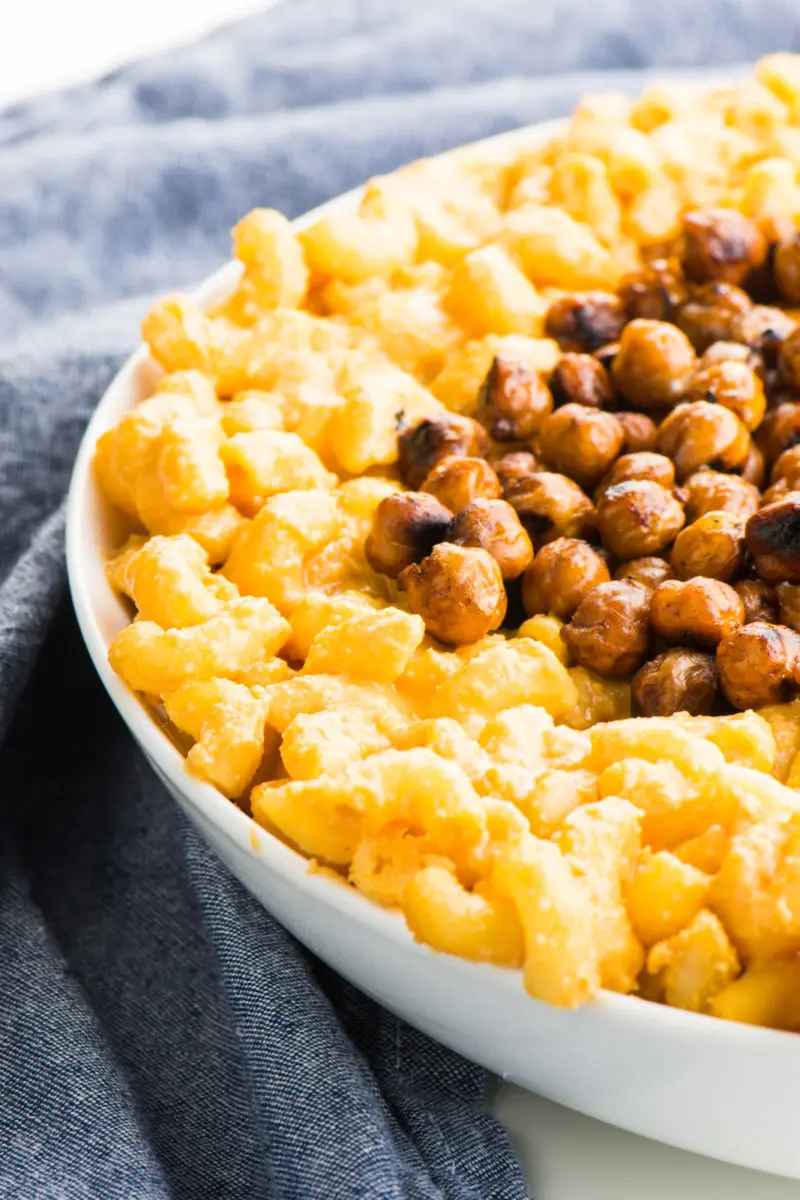 Closeup of Vegan Stovetop Mac and Cheese with Smoky Chickpeas in a white bowl next to a blue kitchen towel