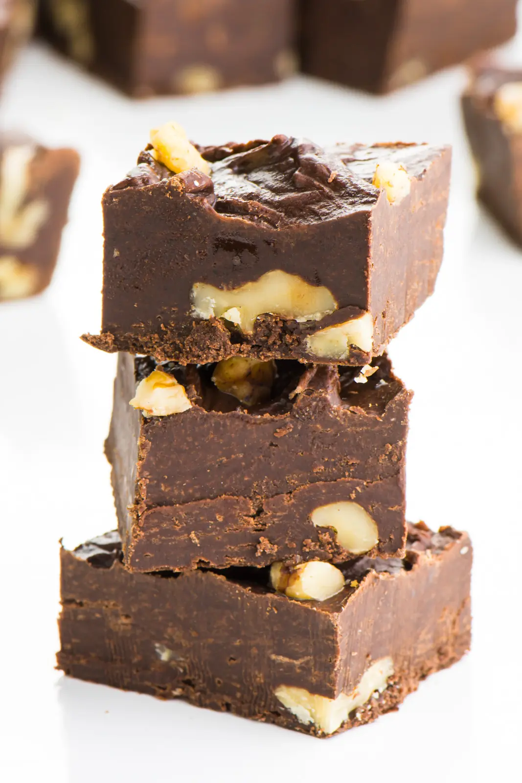 Three pieces of vegan fudge are stacked with more pieces around it.