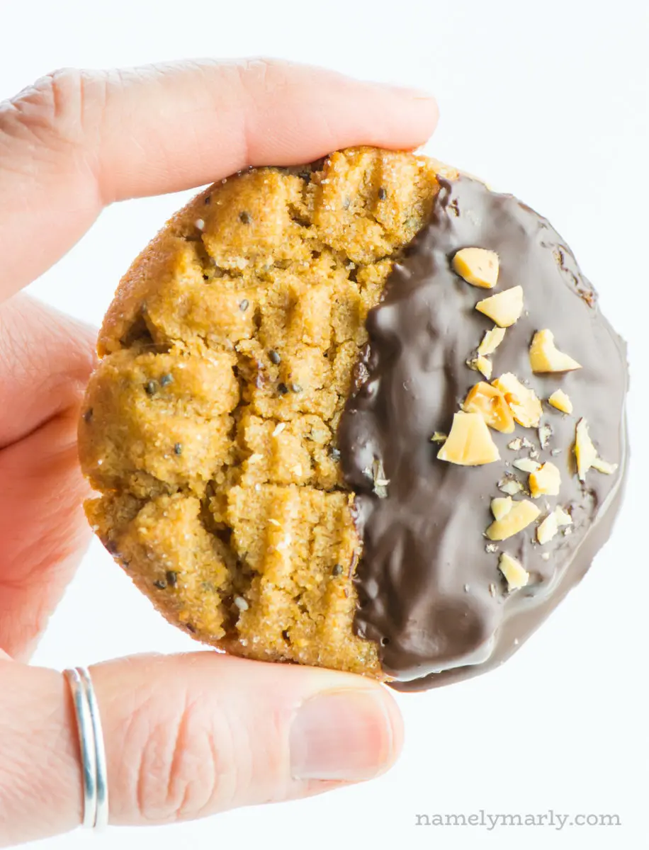 A single chocolate-dipped peanut butter cookie is held between two fingers, ready to be eaten!