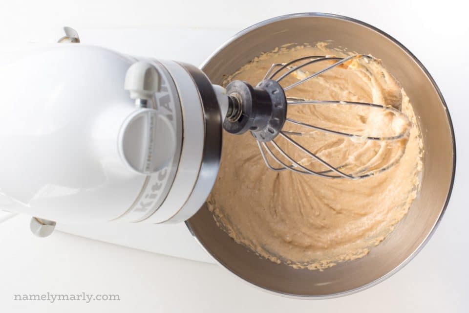 A stand mixer has it's mixing paddle up, with creamy vegan snickerdoodle cookie dough batter in a metal bowl.