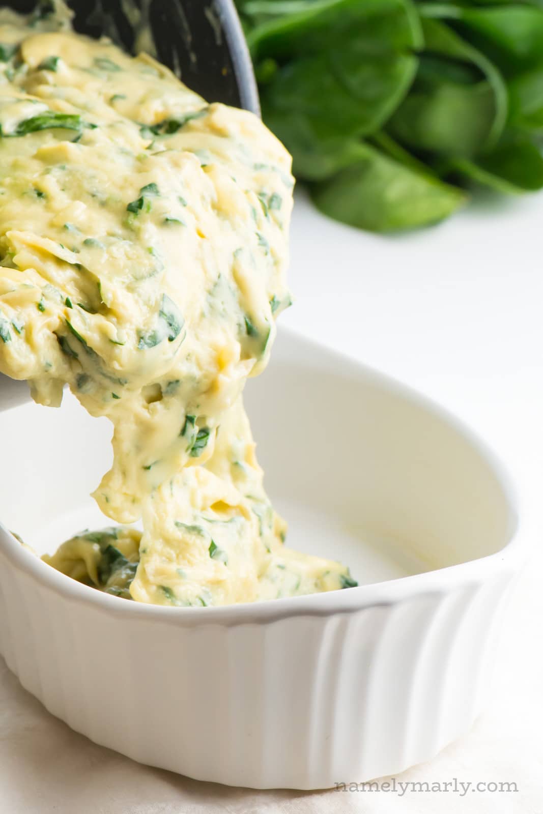 A creamy spinach sauce is being poured from the sauce pan into a serving dish.