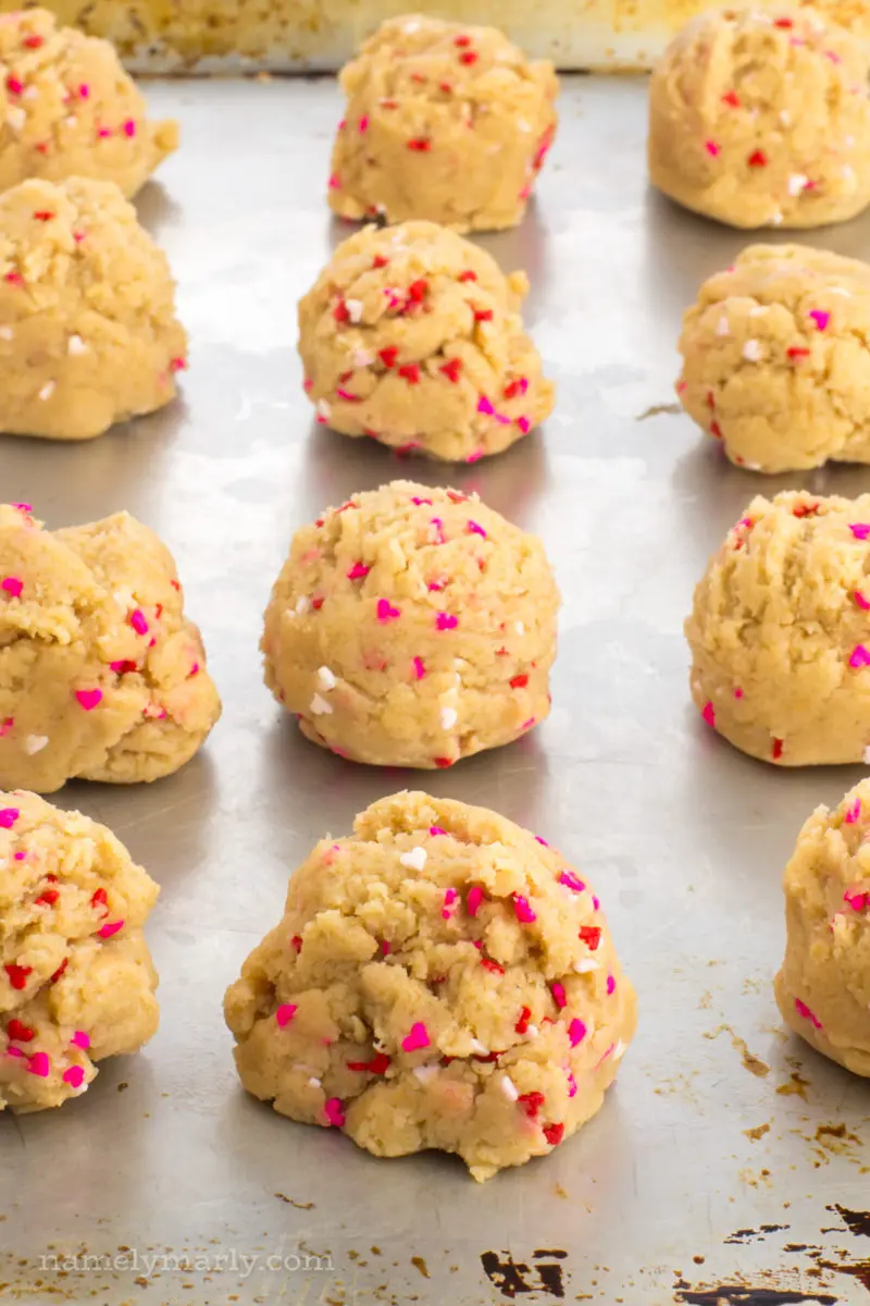 Three rows of valentines cookie dough balls sit next to each other on a baking sheet, getting ready to be placed in the oven.
