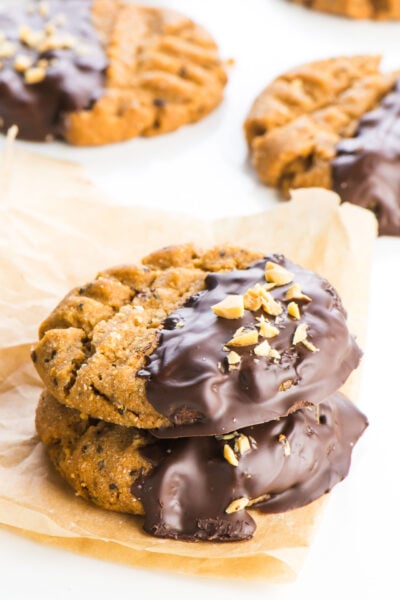 Two cookies are stacked on top of one another, sitting on a piece of brown parchment paper, and two cookies are sitting in the background.