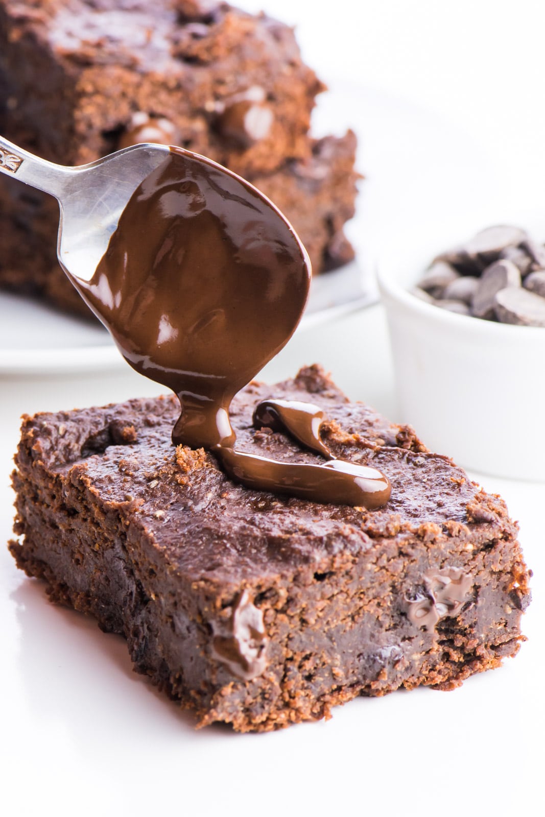 A spoon hovers over a brownie, drizzling melty chocolate over the top. 