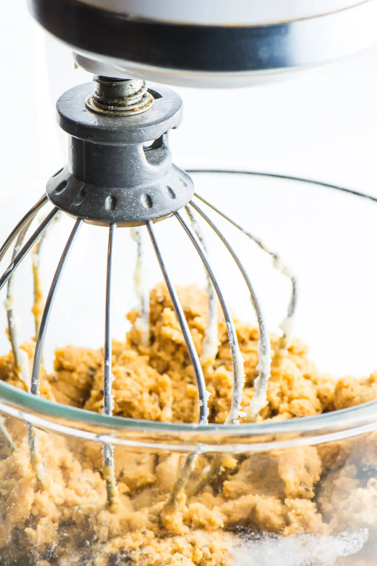 A stand mixer is full of peanut butter cookie dough and is in a glass bowl with the basic mixer attachment.