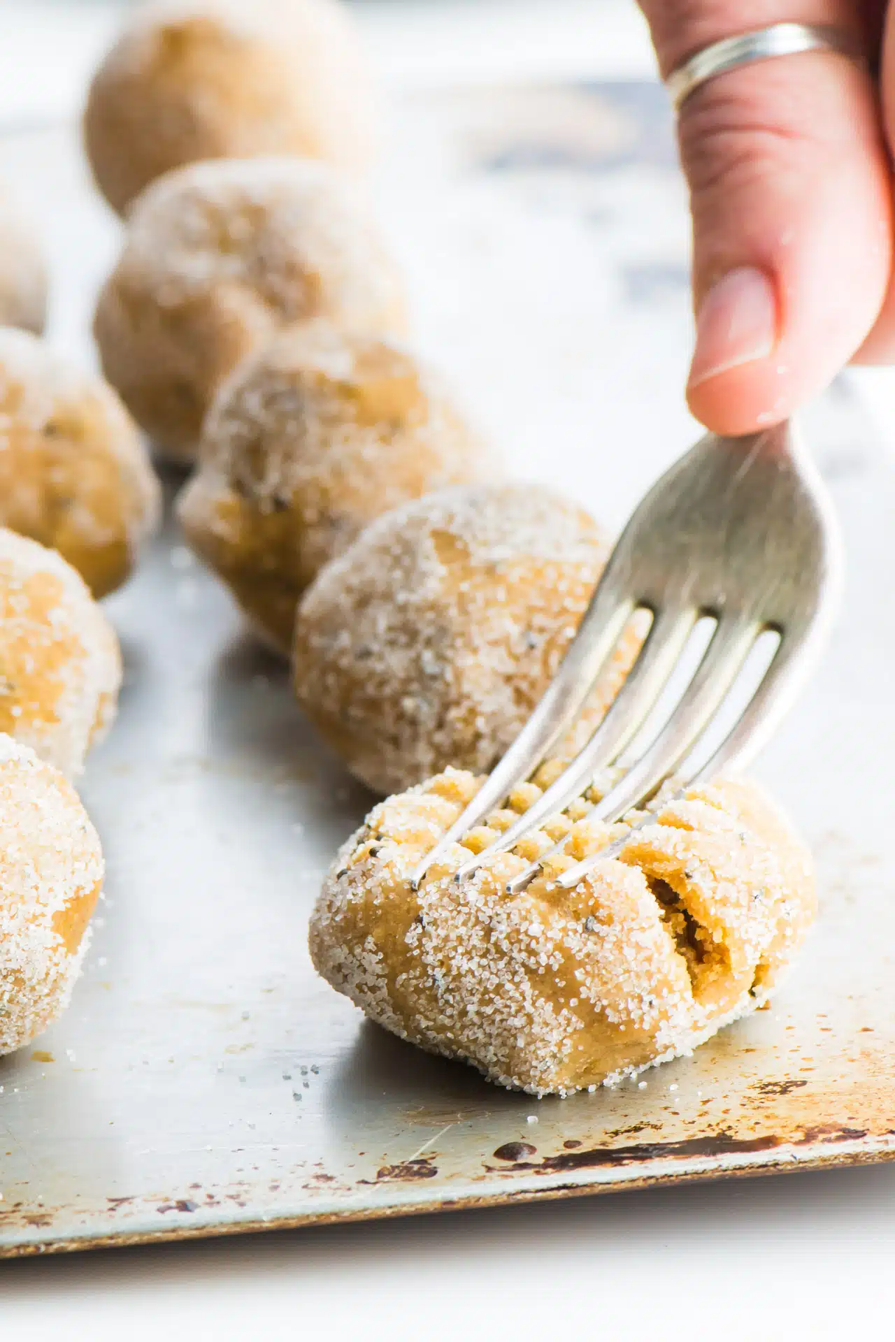 A fork is pressing down on the sugared cookie dough balls, gently pressing them and creating criss-cross indentations in the cookies.