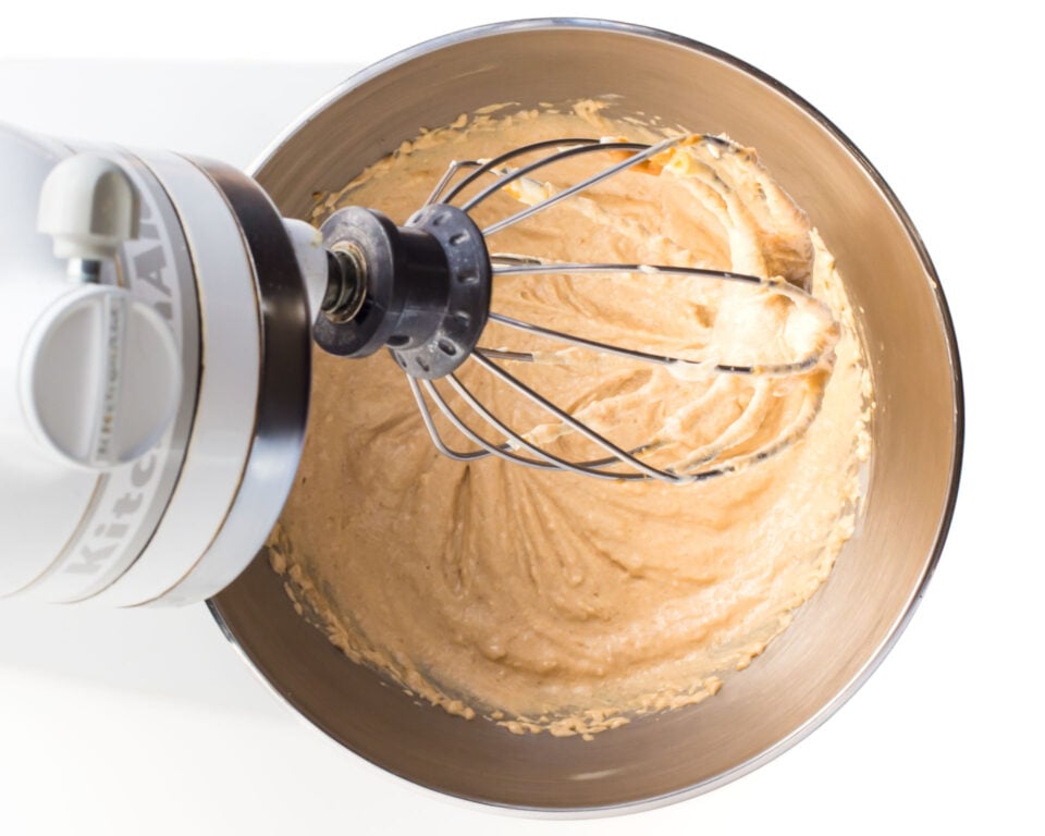 A stand mixer has it's mixing paddle up, with creamy vegan snickerdoodle cookie dough batter in a metal bowl.