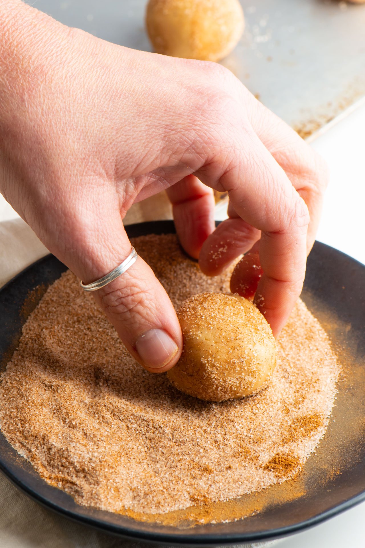 A hand is rolling a vegan snickerdoodle cookie dough ball in a plate full of cinnamon sugar mixed together.