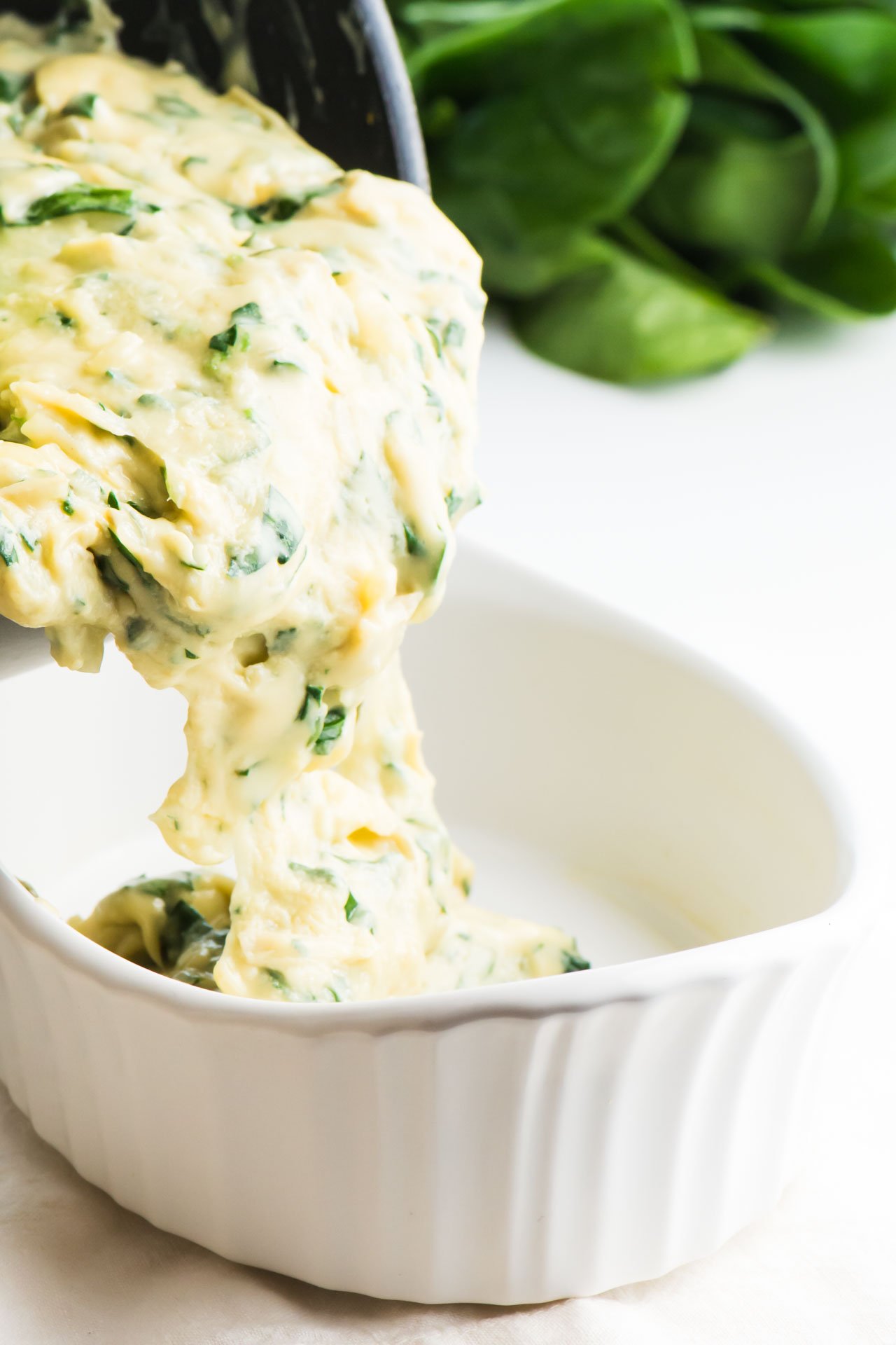 A creamy spinach sauce is being poured from the sauce pan into a serving dish.