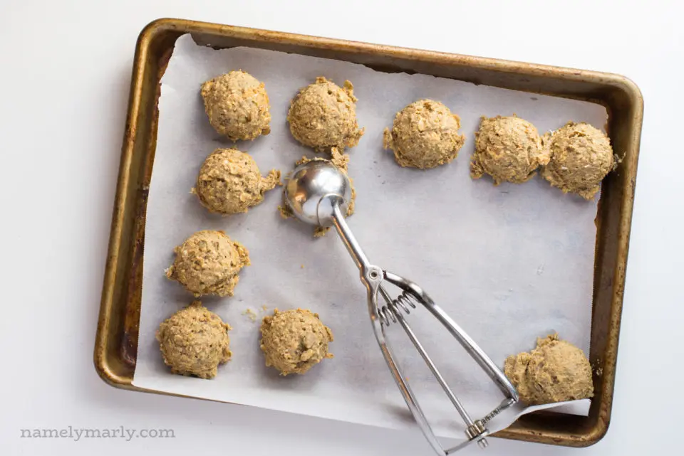 Uncooked lentil burger "meatballs" on a baking sheet with a cookie dough dispenser used to form them.