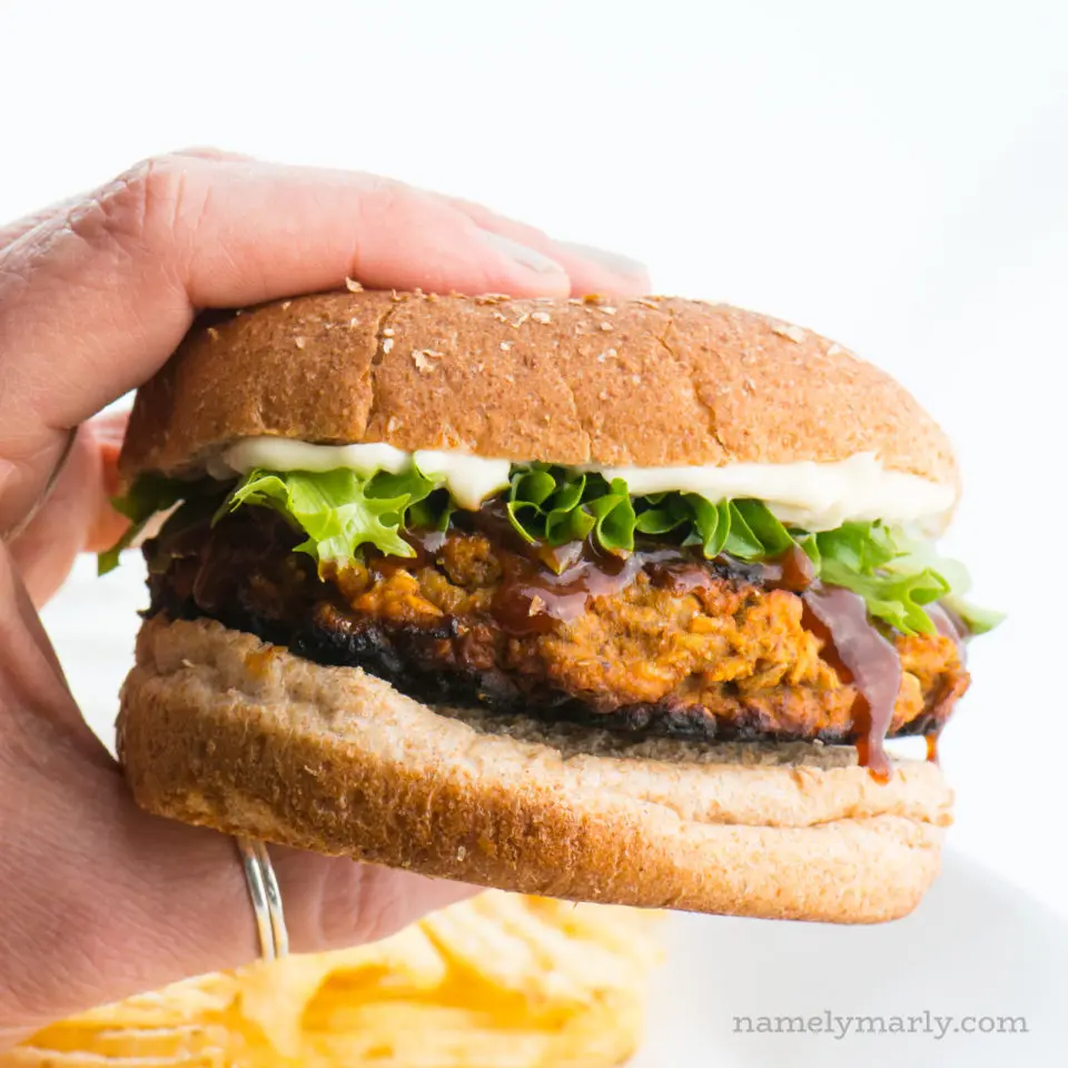 A hand holds a veggie burger, showing off greens and mayo on a whole wheat bun.