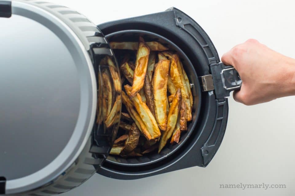 A hand pulls out a tray from an air fryer full of freshly made french fries.