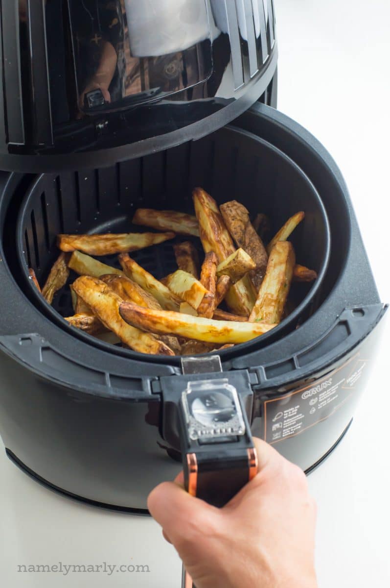 A hand is pulling out the tray holding french fries from an air fryer.