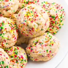 A white plate has several colorful confetti cookies, sugar cookies with sprinkles baked right into the dough.