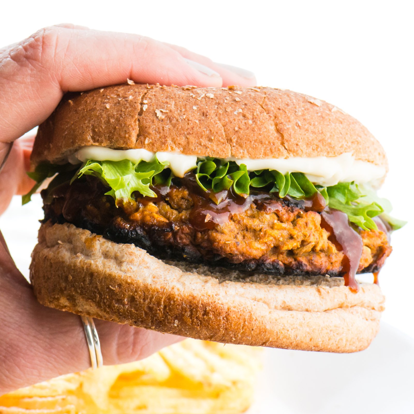 A hand holds a lentil burger, showing off greens and mayo on a whole wheat bun.