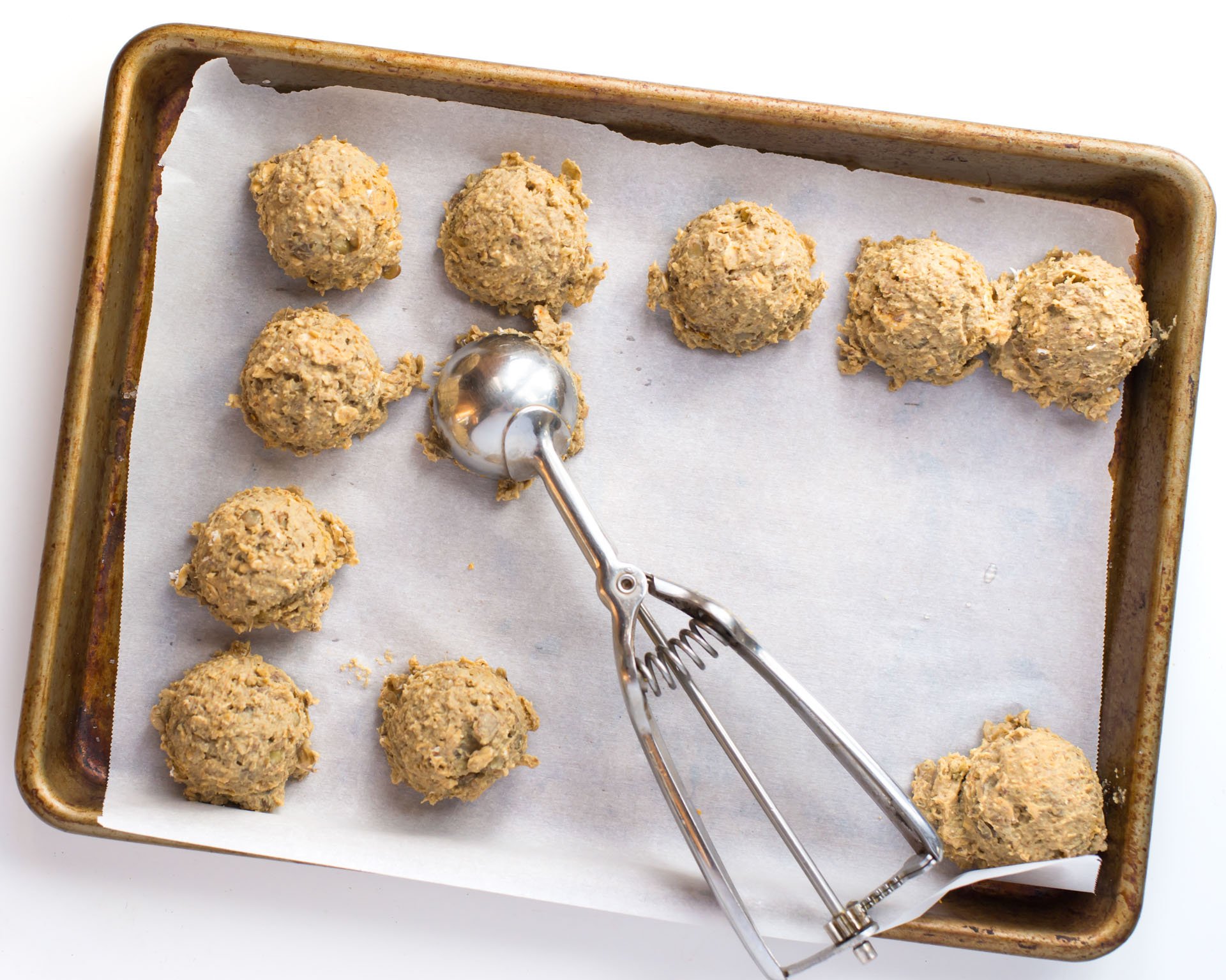 Uncooked lentil burger "meatballs" on a baking sheet with a cookie dough dispenser used to form them.