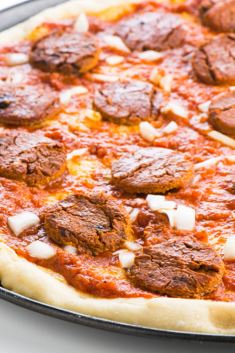 Homemade Vegan Pepperoni is sliced and placed on a pizza with chopped onions. There is no cheese on this pizza to better highlight the pepperoni slices.