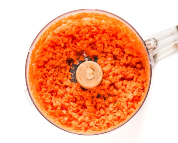 Freshly ground carrots are in the bowl of a food processor.