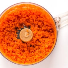 Freshly ground carrots are in the bowl of a food processor.
