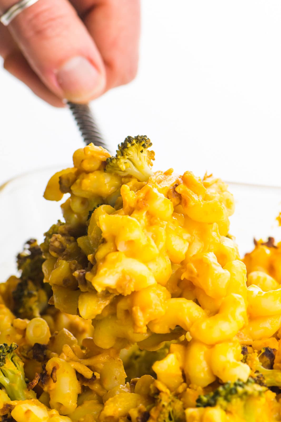 A hand reaches in and scoops out some vegan mac and cheese casserole from the dish.
