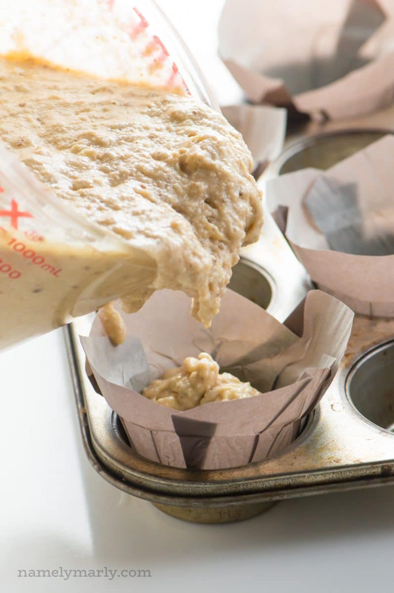 The measuring glass is being used to pour muffin batter into papers in a muffin tin.