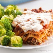 A slice of lasagna on a plate with steamed broccoli beside it.