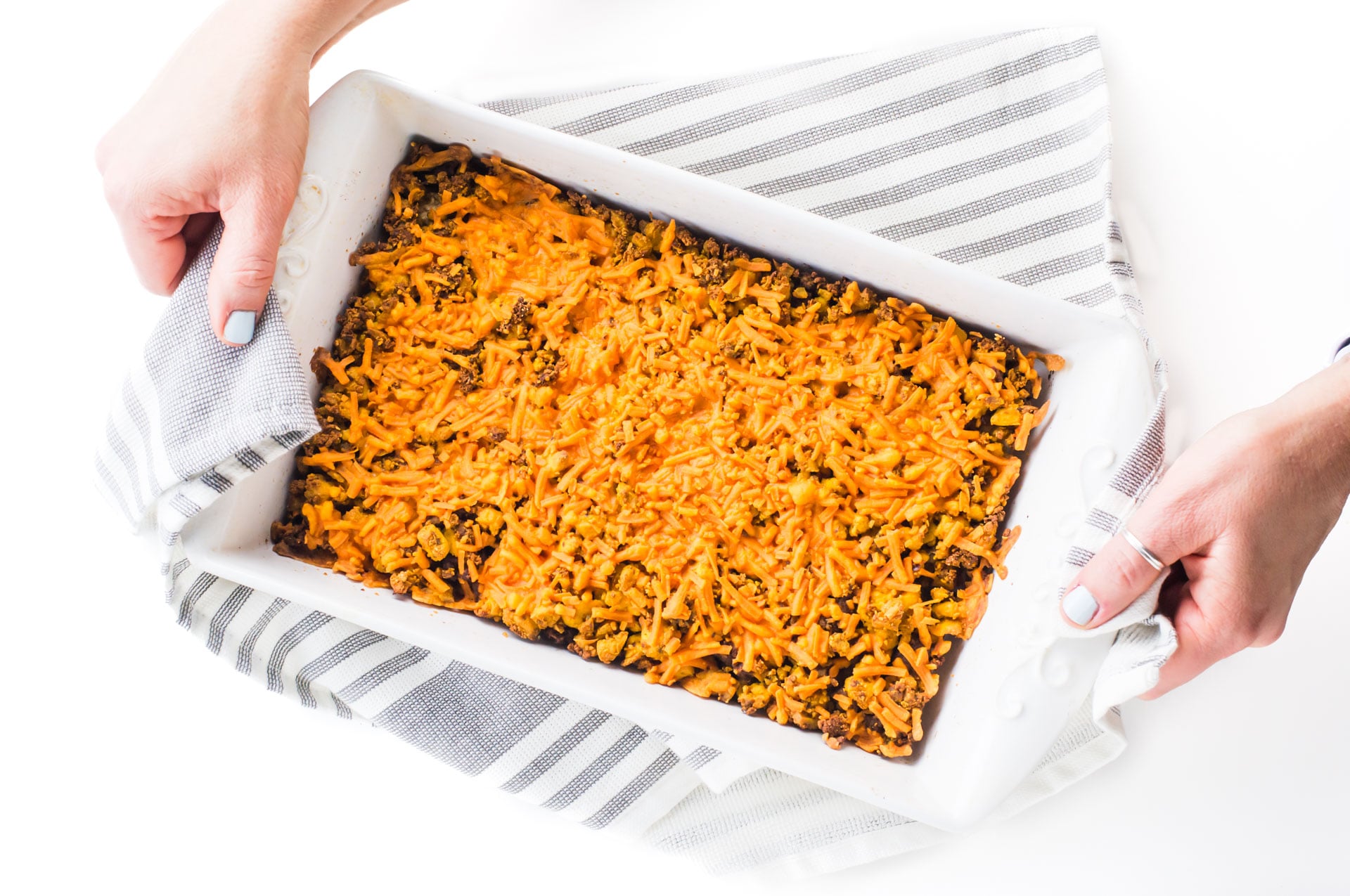 Hands are using a kitchen towel to hold this breakfast casserole dish.
