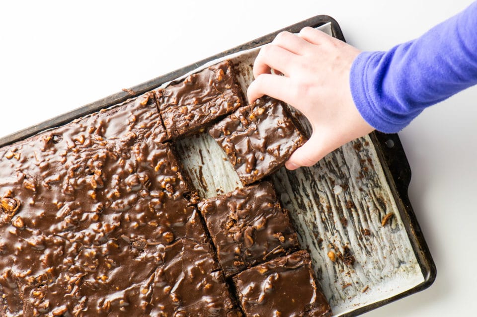A hand reaches to grab a slice of this vegan Texas sheet cake straight from the pan!