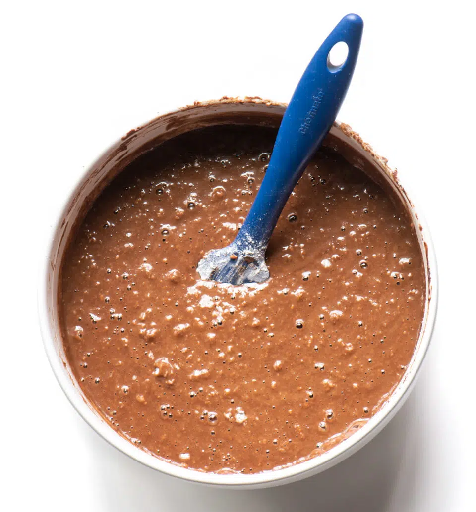 A bowl of chocolate batter has a blue spatula in it for stirring.
