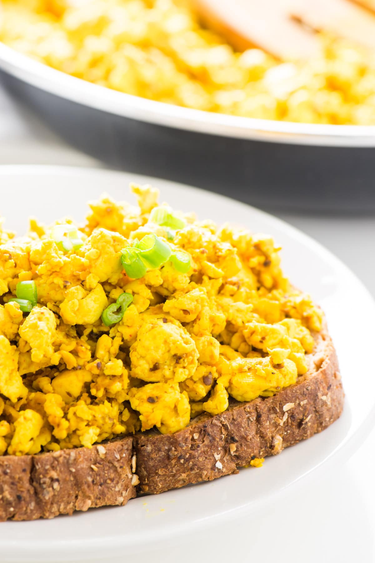 Vegan egg scrambled on a piece of toast with more in a skillet behind it.