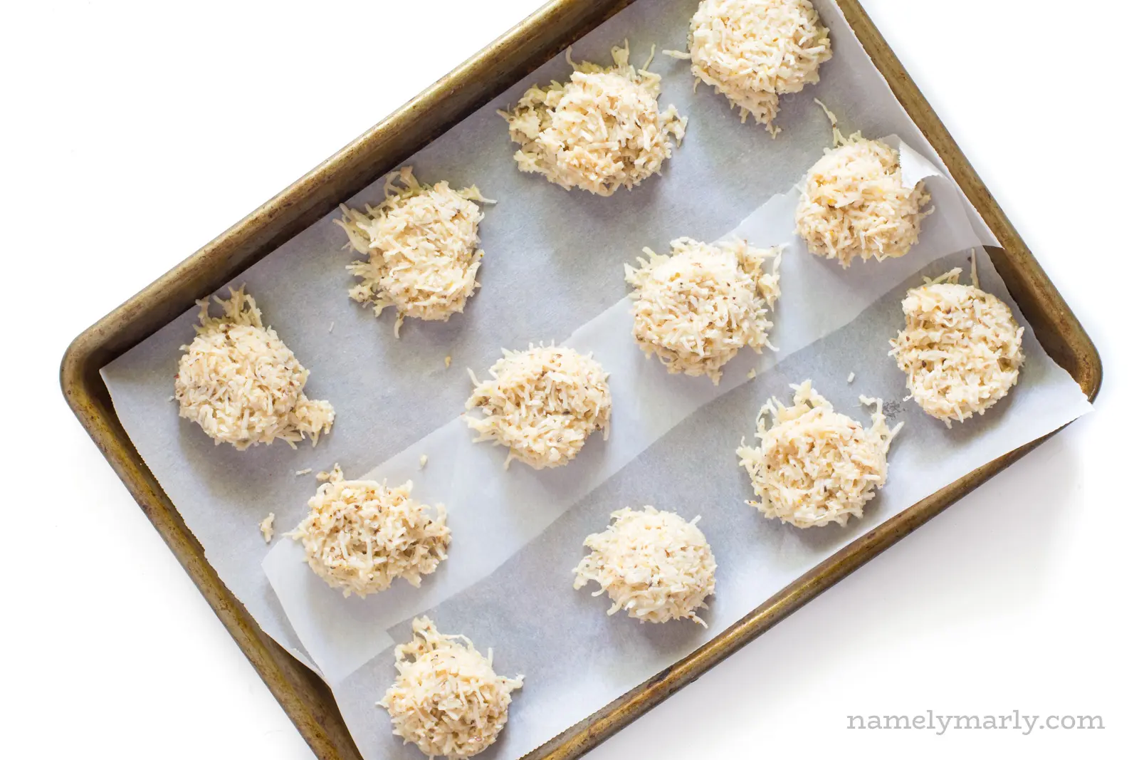 Uncooked coconut macaroons are lined up in a baking sheet lined with parchment paper.