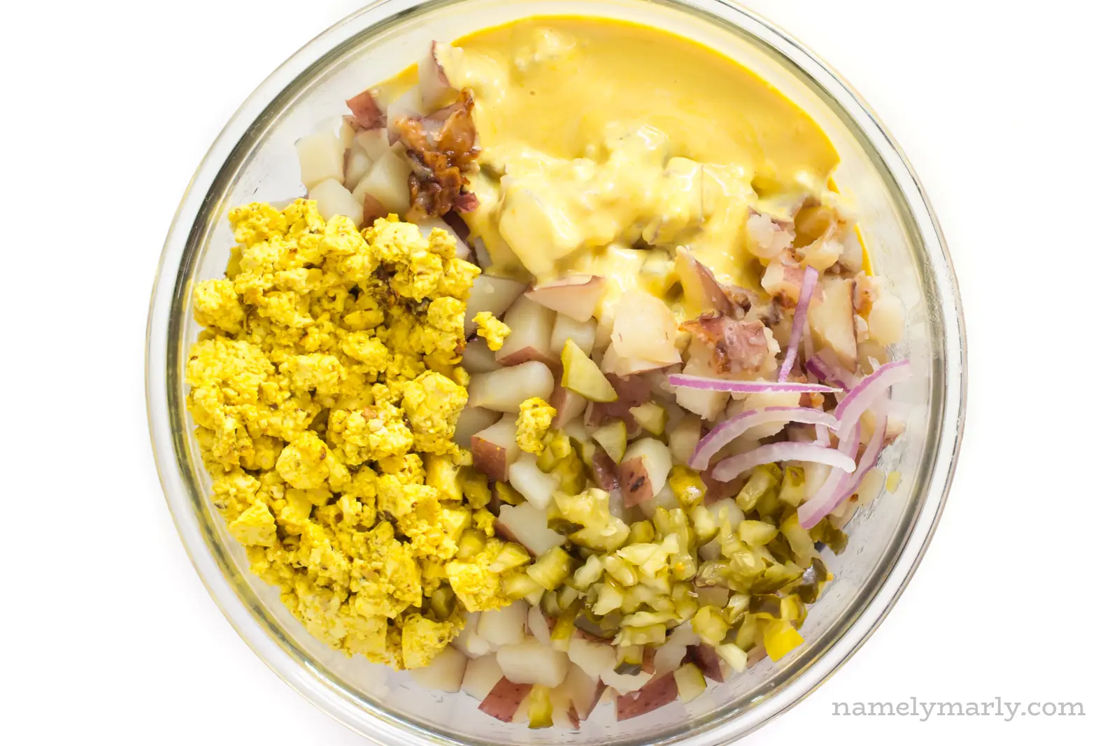A bowl contains the ingredients, like potatoes, onions, and sauce for vegan potato salad.