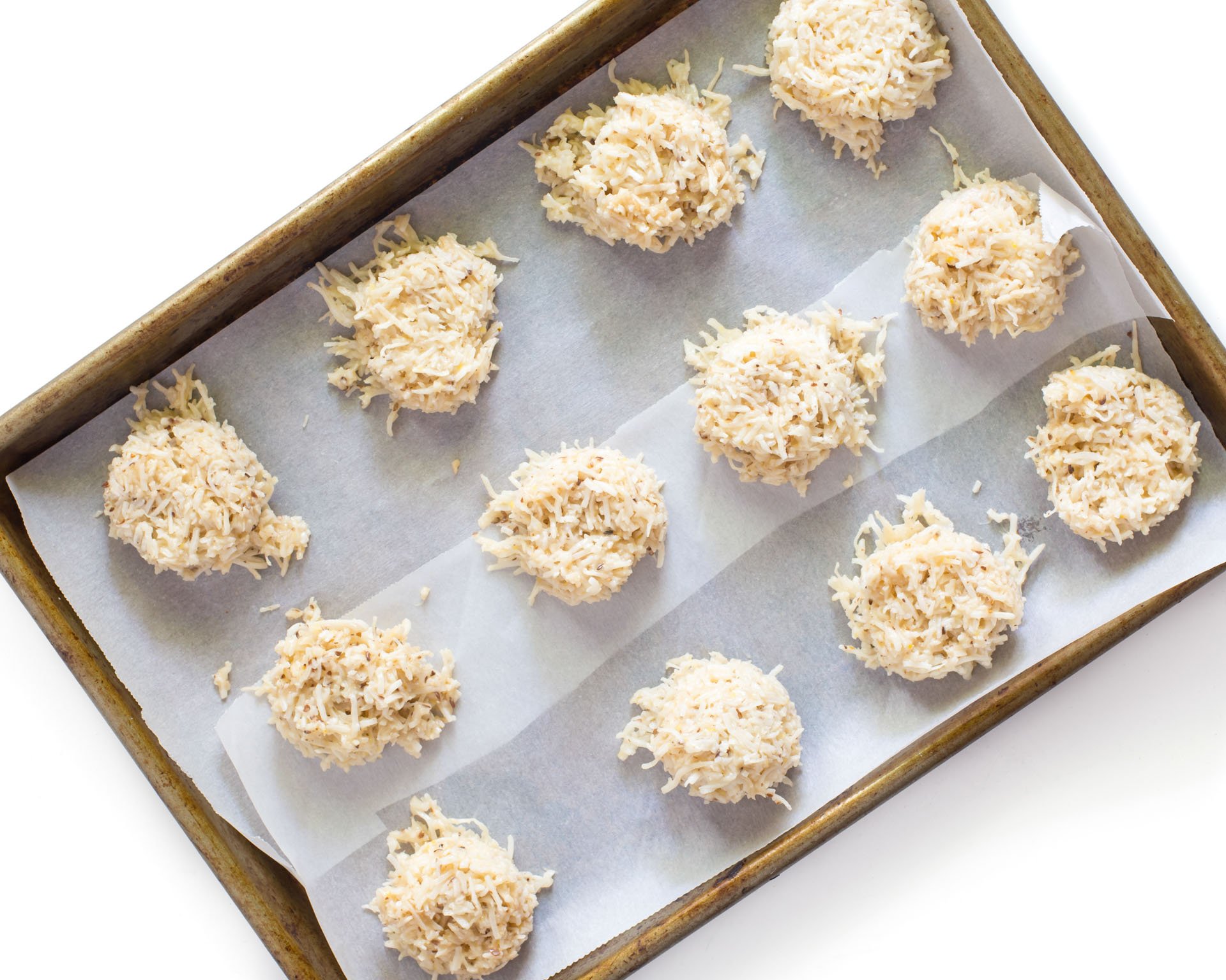 Uncooked coconut macaroons are lined up in a baking sheet lined with parchment paper.