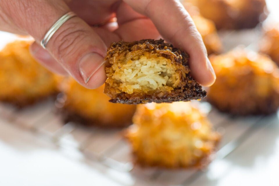 A hand holds a macaroon cookies with a bite taken out.