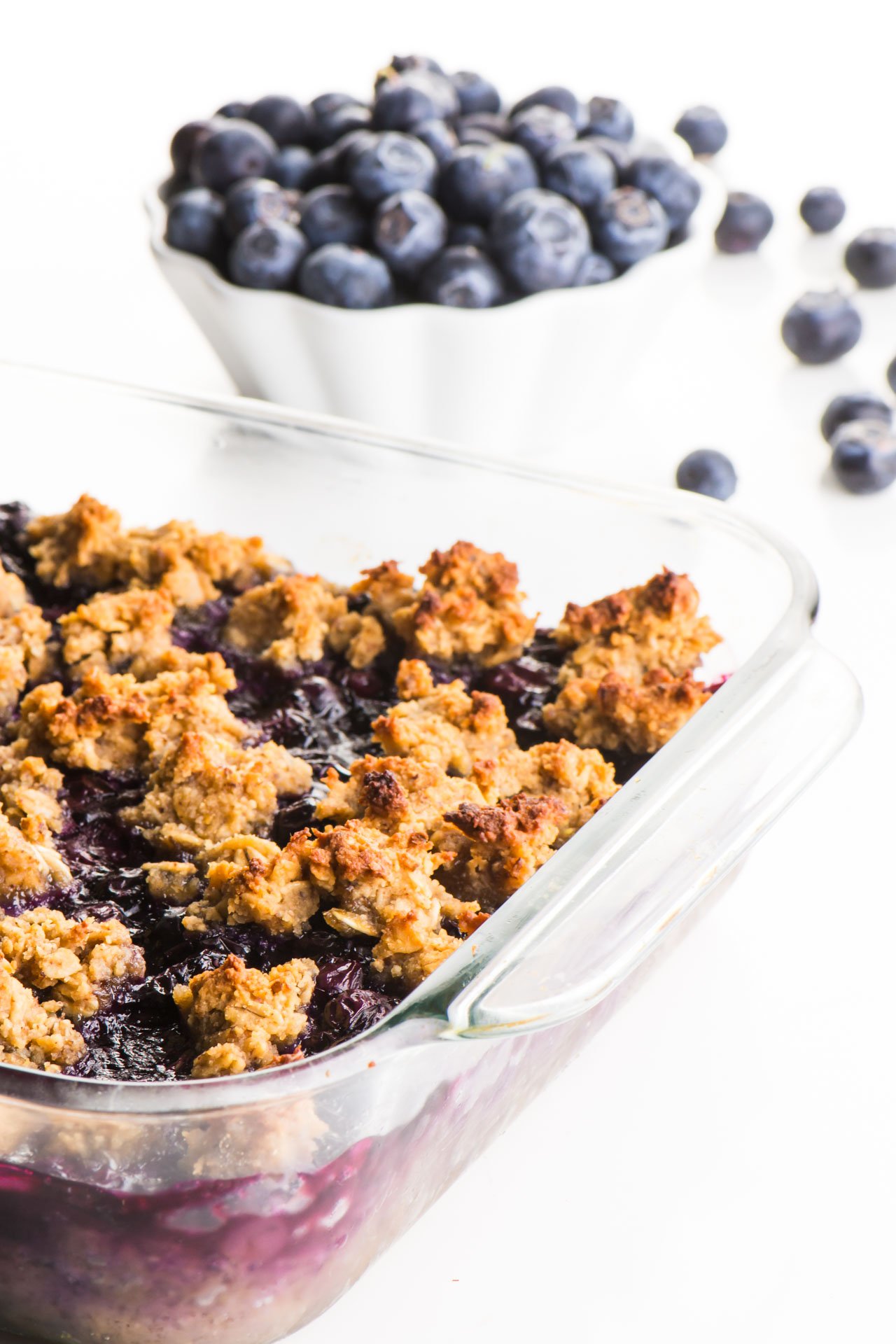 A baking dish full of blueberry crumble bars sits next to a bowl of fresh blueberries.