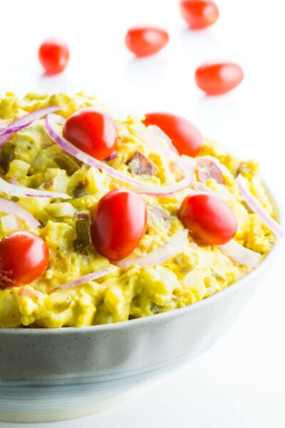 A bowl of vegan potato salad with cherry tomatoes on the salad and behind it.