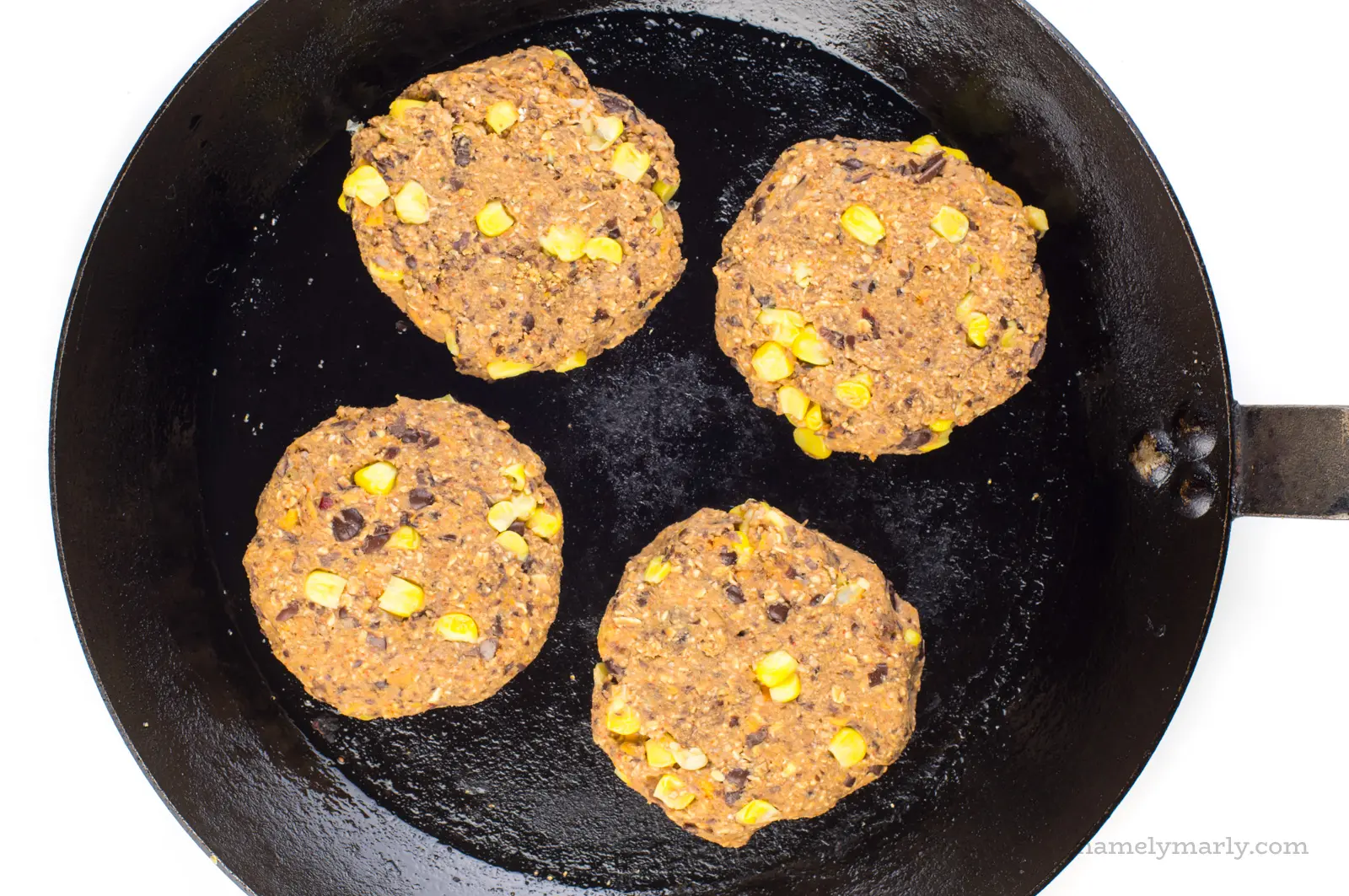 Black bean burger patties with fresh corn are cooking on a skillet.