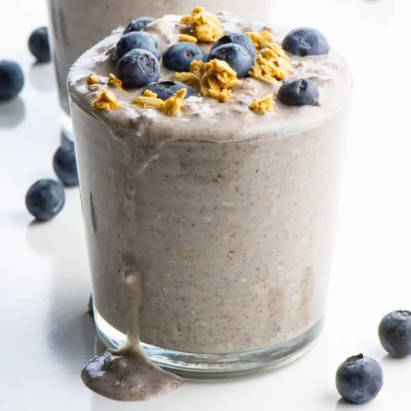 The glass of overnight oats is topped with fresh blueberries and granola.