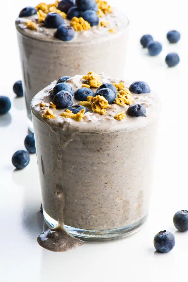 The blueberry overnight oats is in a glass and oozing over the side.