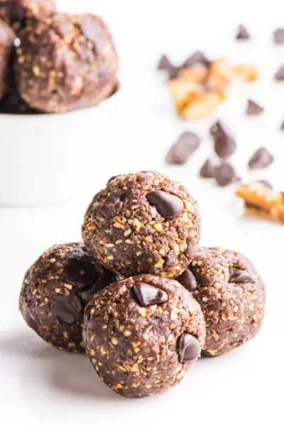 Chocolate energy balls are grouped together with more in a bowl behind them.