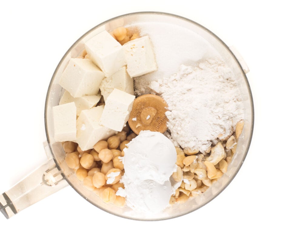The ingredients for vegan cheesecake are in the bottom of a food processor.