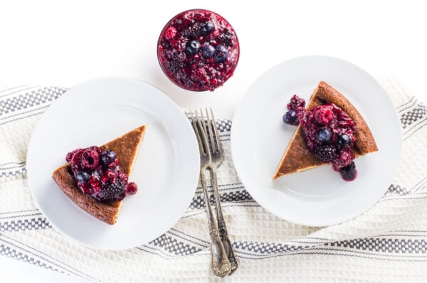 Looking down on plated slices of dairy free cheesecake with berry filling in a bowl between them.
