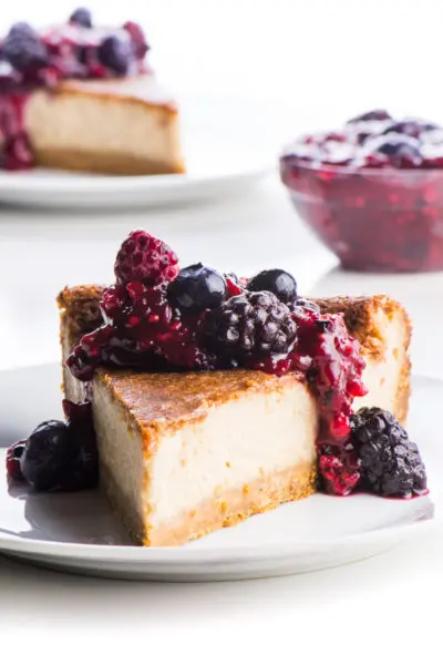 A slice of dairy free cheesecake sits on a white plate with berry sauce drizzled over the top.