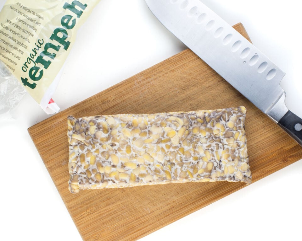 A block of tempeh on a cutting board next to a knife.