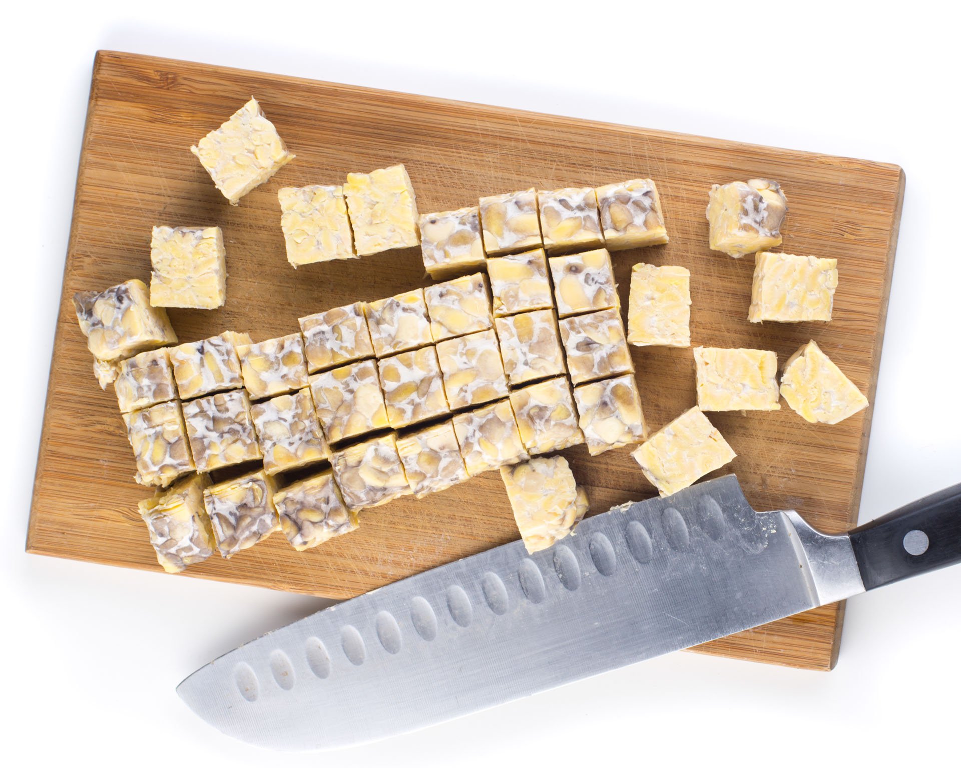 Tempeh chopped into cubes sitting next to a knife on a cutting board.
