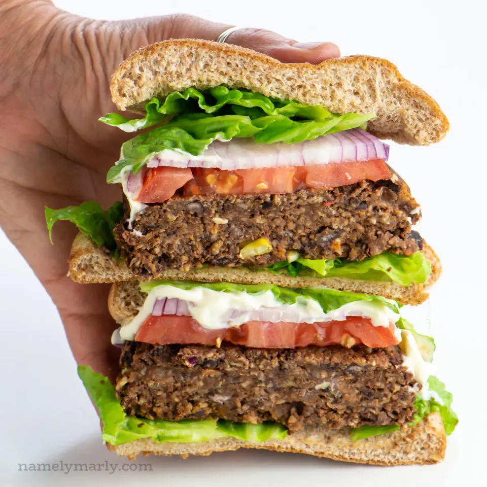 A hand holds two halves of a black bean burger stacked on top of each other.