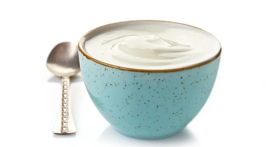 A blue bold is full of creamy, white yogurt. A silver spoon sits beside the bowl.