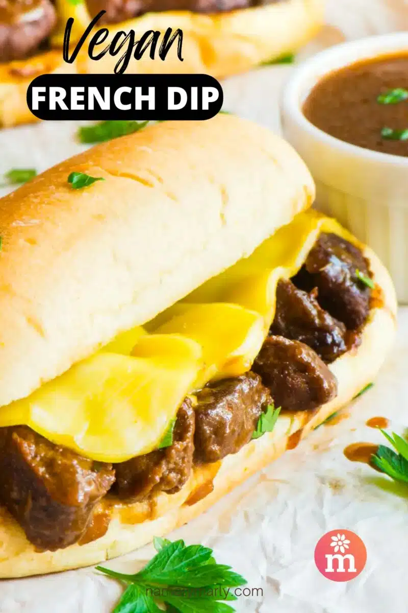 A sandwich with plant-based meat and cheese sits in front of a bowl of gravy. The text reads, Vegan French Dip